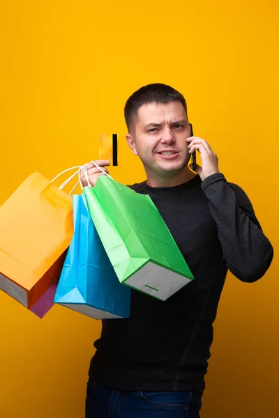 Foto do homem comprador com sacos de papel, cartão de banco e telefone na mão — Fotografia de Stock