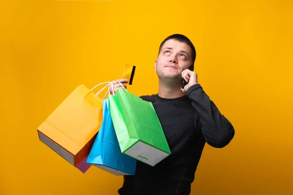 Foto do homem comprador com sacos de papel, cartão de banco e telefone na mão — Fotografia de Stock
