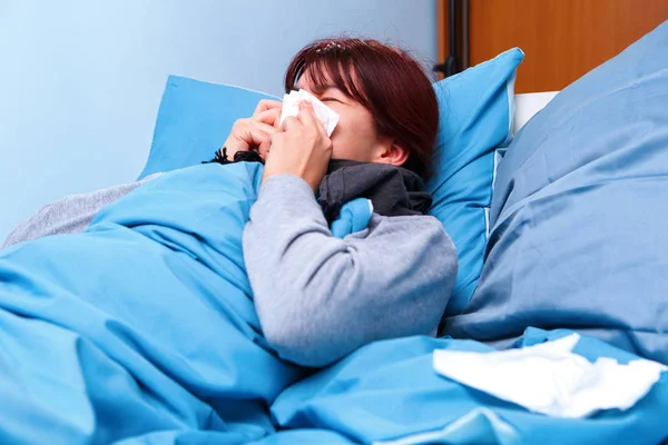 Foto sisi gadis berambut cokelat yang sakit meniup hidungnya di saputangan kertas berbaring di tempat tidur  . — Stok Foto