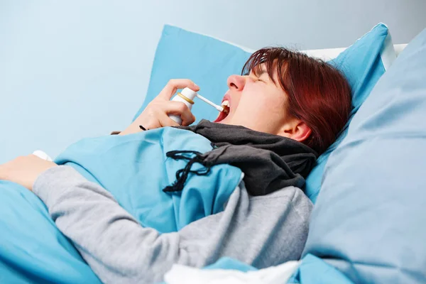 Imagem de morena doente usando spray de garganta deitada na cama  . — Fotografia de Stock