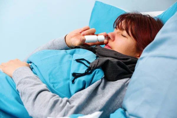 Foto de mujer enferma usando aerosol nasal acostada en la cama —  Fotos de Stock