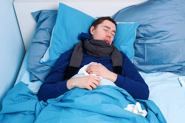 Foto de homem doente em cachecol e com lenços deitados na cama . — Fotografia de Stock