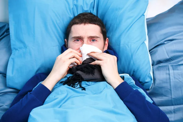 Φωτογραφία άρρωστου άντρα με μαντήλι που κάθεται στο κρεβάτι — Φωτογραφία Αρχείου