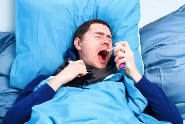 Kép a tüsszgő beteg ember sálat és zsebkendő a kezében feküdt az ágyban . — Stock Fotó