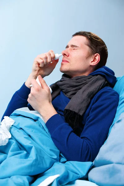 Side photo of sick brunet male using nasal spray while lying in bed. — Stock Photo, Image