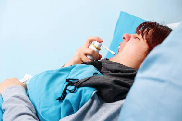 Imagem de morena doente usando spray de garganta deitada na cama  . — Fotografia de Stock