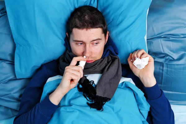 Άρρωστος Μπρουνέ άνθρωπος χρησιμοποιώντας ρινικό σπρέι, ενώ ξαπλωμένο στο κρεβάτι — Φωτογραφία Αρχείου