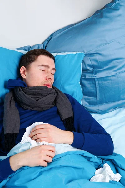 Foto de homem doente em cachecol e com lenços deitados na cama . — Fotografia de Stock