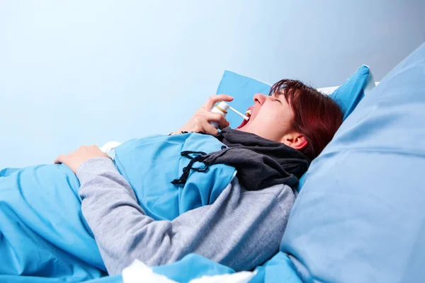 Εικόνα άρρωστο μελαχρινή χρησιμοποιώντας σπρέι λαιμό ξαπλωμένη στο κρεβάτι . — Φωτογραφία Αρχείου