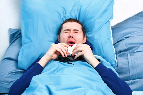 Foto av nysningar sjuk man i halsduk och med näsdukar liggande i sängen. — Stockfoto