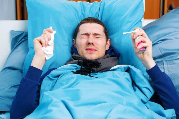 Φωτογραφία του άρρωστου άντρα με κασκόλ με μαντήλι και σπρέι με φάρμακα που βρίσκονται στο κρεβάτι. — Φωτογραφία Αρχείου