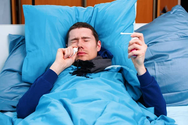Foto de hombre moreno enfermo en bufanda con pañuelo y spray con medicina acostado en la cama  . —  Fotos de Stock
