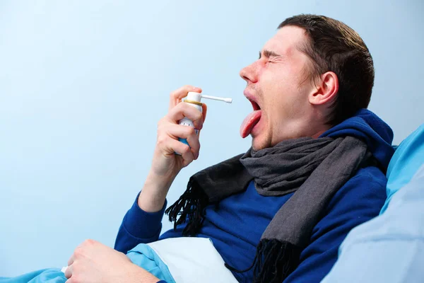 Фотографія хворого чоловіка в шарфі з використанням спрею з ліками для горла, що лежить у ліжку — стокове фото