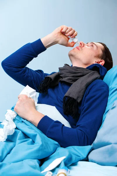 Boczne zdjęcie chorych Brunet człowiek za pomocą aerozolu do nosa, leżąc w łóżku. — Zdjęcie stockowe