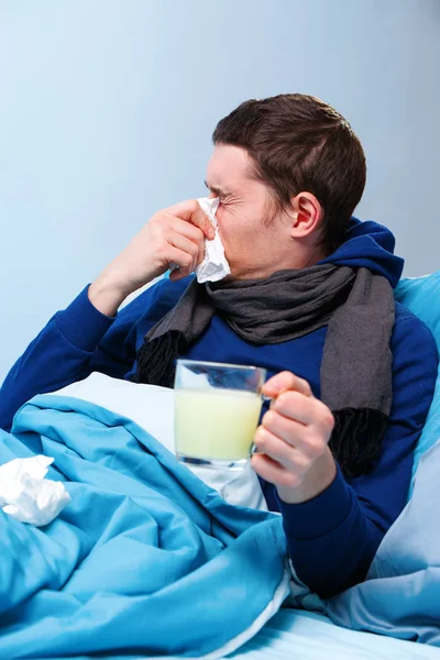 Zdjęcie chore człowieka w szalik z filiżanką medycyny leżącej w łóżku — Zdjęcie stockowe