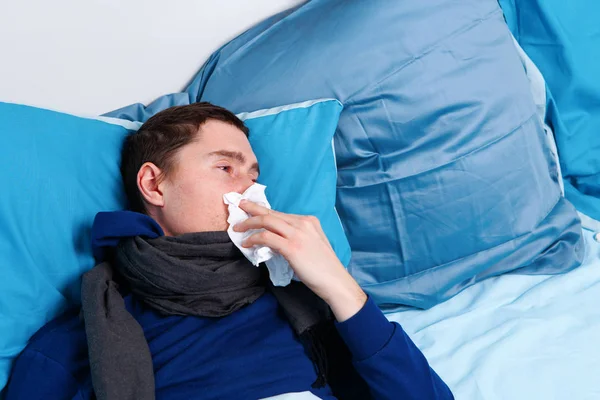 Imagen del hombre moreno enfermo en bufanda y con pañuelos acostados en la cama  . —  Fotos de Stock