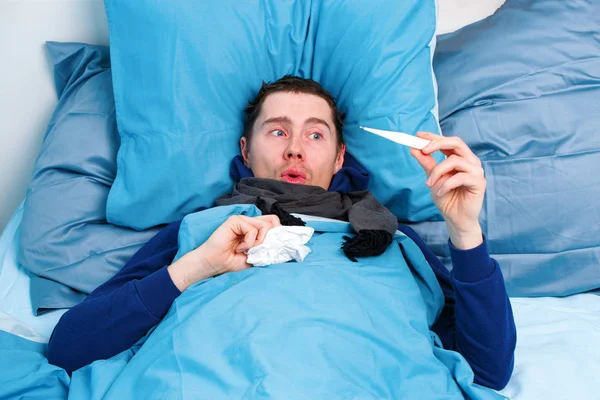 Uomo brunetta malato in sciarpa con termometro in mano sdraiato a letto . — Foto Stock