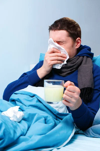 Foto de homem doente em cachecol com xícara de remédio deitado na cama — Fotografia de Stock