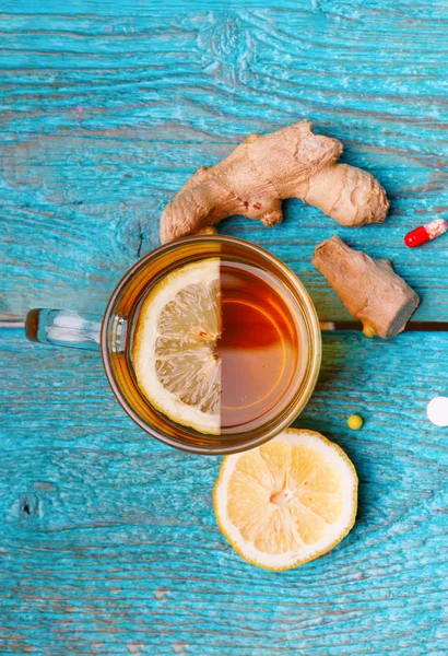 Cold medicines, tea, lemon and ginger on wooden blue background