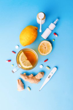Mavi arka planda soğuk preparatlar, termometre, çay, limon ve zencefil.