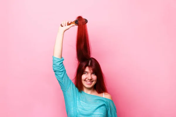 Woman brushing her hair on pink background — Stock Photo, Image
