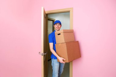 Photo of courier man in blue baseball cap with cardboard boxes in hands. clipart