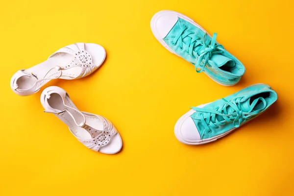 A pair of white high-heeled sandals and a pair of turquoise sneakers on yellow background