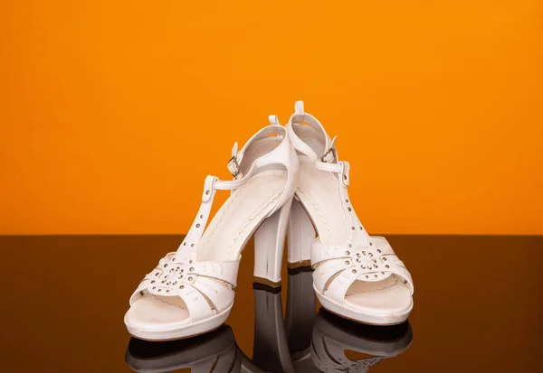 White sandals with high heel on black glass table and yellow background.