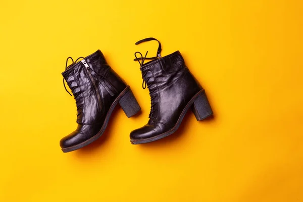 Elegant women black heeled boots. Top view of black boots on a yellow background.