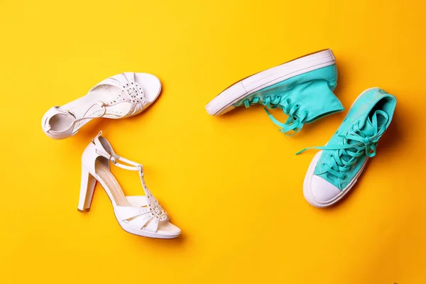 A pair of white high-heeled sandals and a pair of turquoise sneakers on yellow background