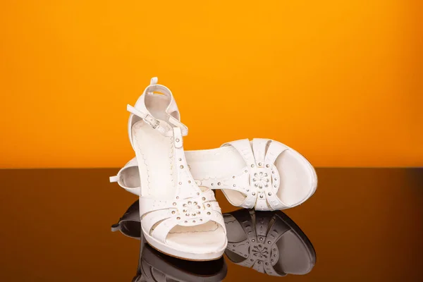 Hvite sandaler med høy hæl på svart glassbord og gul bakgrunn . – stockfoto