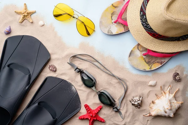 Gafas de natación, aletas, chanclas, gafas de sol y sombrero en la arena con conchas y estrellas de mar . — Foto de Stock