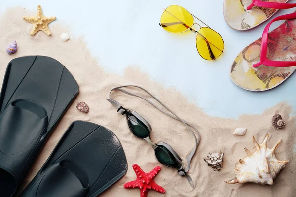 Gafas de natación, aletas, chanclas, gafas de sol y sombrero en la arena con conchas y estrellas de mar . — Foto de Stock