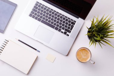 Not defteri, tablet, boş defter, yeşil çiçek ve kahve dolu beyaz masa.