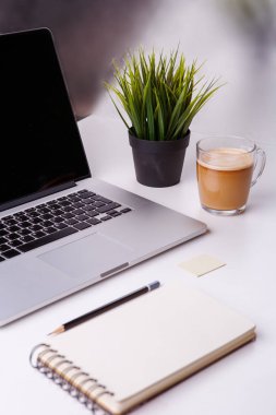 Not defterli beyaz masa, boş defter, yeşil çiçek ve bir fincan kahve..