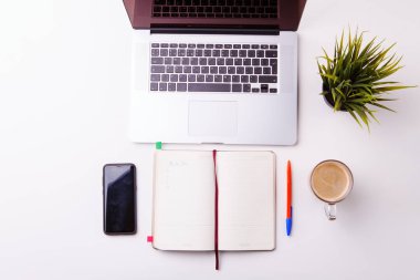 Not defteri, tablet, boş defter, yeşil çiçek, telefon ve kahve dolu beyaz masa.