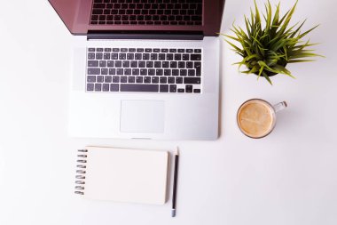 Not defteri, tablet, boş defter, yeşil çiçek ve kahve dolu beyaz masa.