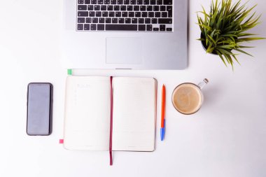 Not defteri, tablet, boş defter, yeşil çiçek, telefon ve kahve dolu beyaz masa.