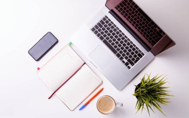 Not defteri, tablet, boş defter, yeşil çiçek, telefon ve kahve dolu beyaz masa.
