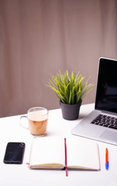 Not defterli beyaz masa, boş defter, yeşil çiçek, telefon ve bir fincan kahve..