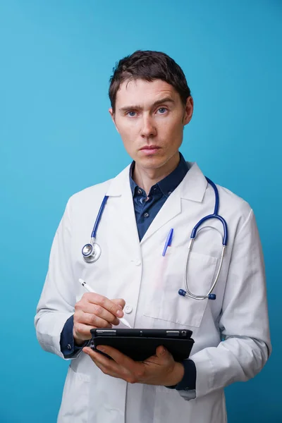 Portrait of doctor with stethoscope and tablet computer in hand on blue background — Stock Photo, Image