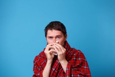 Battaniyeye sarılmış hasta bir adam burnunu beyaz mendille üflüyor.