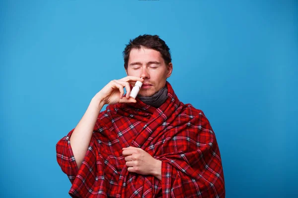 Un avvolto in una coperta malato è in piedi e utilizzando spray nasale — Foto Stock