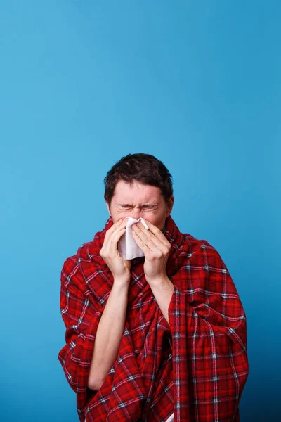 Um enrolado num cobertor doente está a assoar o nariz com um lenço branco. — Fotografia de Stock