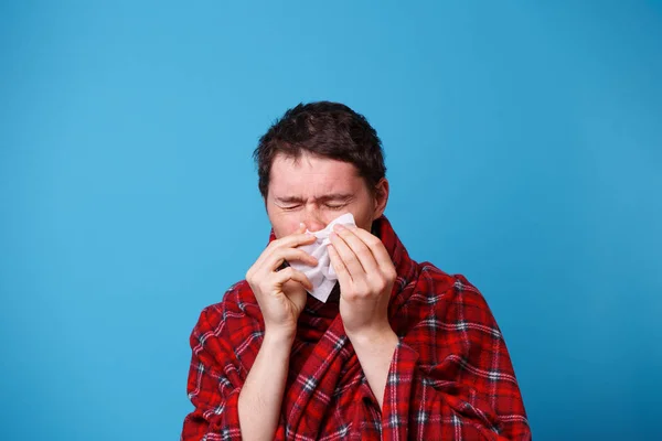 Um enrolado num cobertor doente está a assoar o nariz com um lenço branco. — Fotografia de Stock