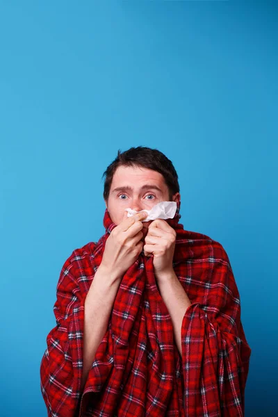 Un uomo malato avvolto in una coperta si sta soffiando il naso nel fazzoletto bianco — Foto Stock