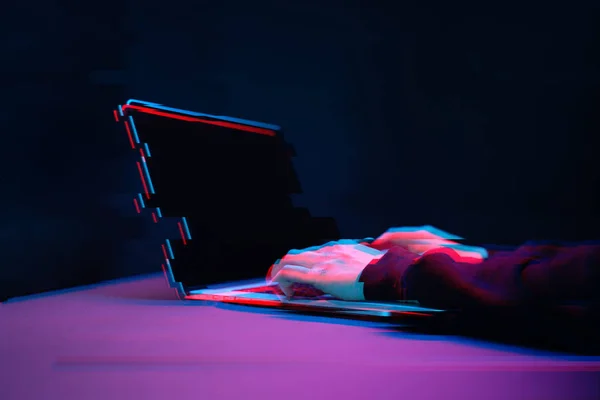 Hacker w kaptur pracy z laptopem wpisując tekst w ciemnym pomieszczeniu. Obraz z efektem glitch — Zdjęcie stockowe