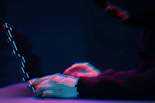 Hacker no capô trabalhando com laptop digitando texto no quarto escuro. Imagem com efeito de falha — Fotografia de Stock