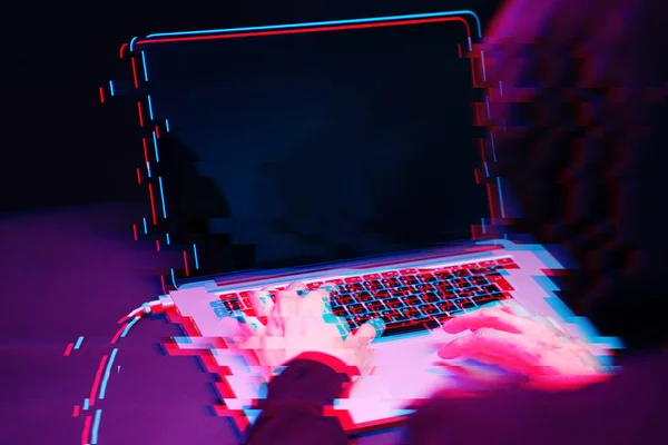 Hacker in the hood working with laptop typing text in dark room. Image with glitch effect — Stock Photo, Image