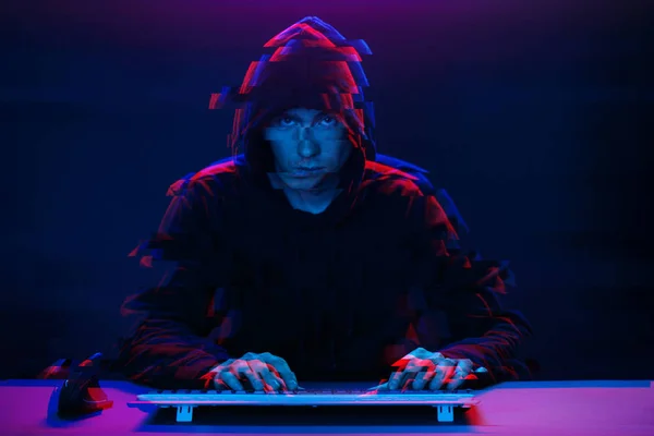 Hacker dans le capot travaillant avec l'ordinateur tapant du texte dans la pièce sombre. Image avec effet de pépin — Photo